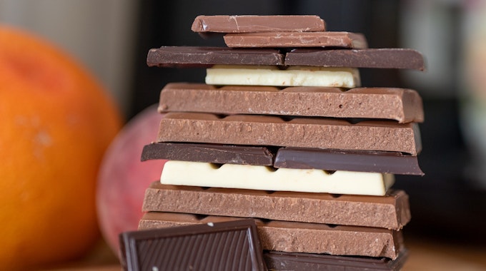 Stücke von Vollmilchschokolade, weißer Schokolade und Zartbitterschokolade liegen auf einem Holzbrett in der Küche.&nbsp;
