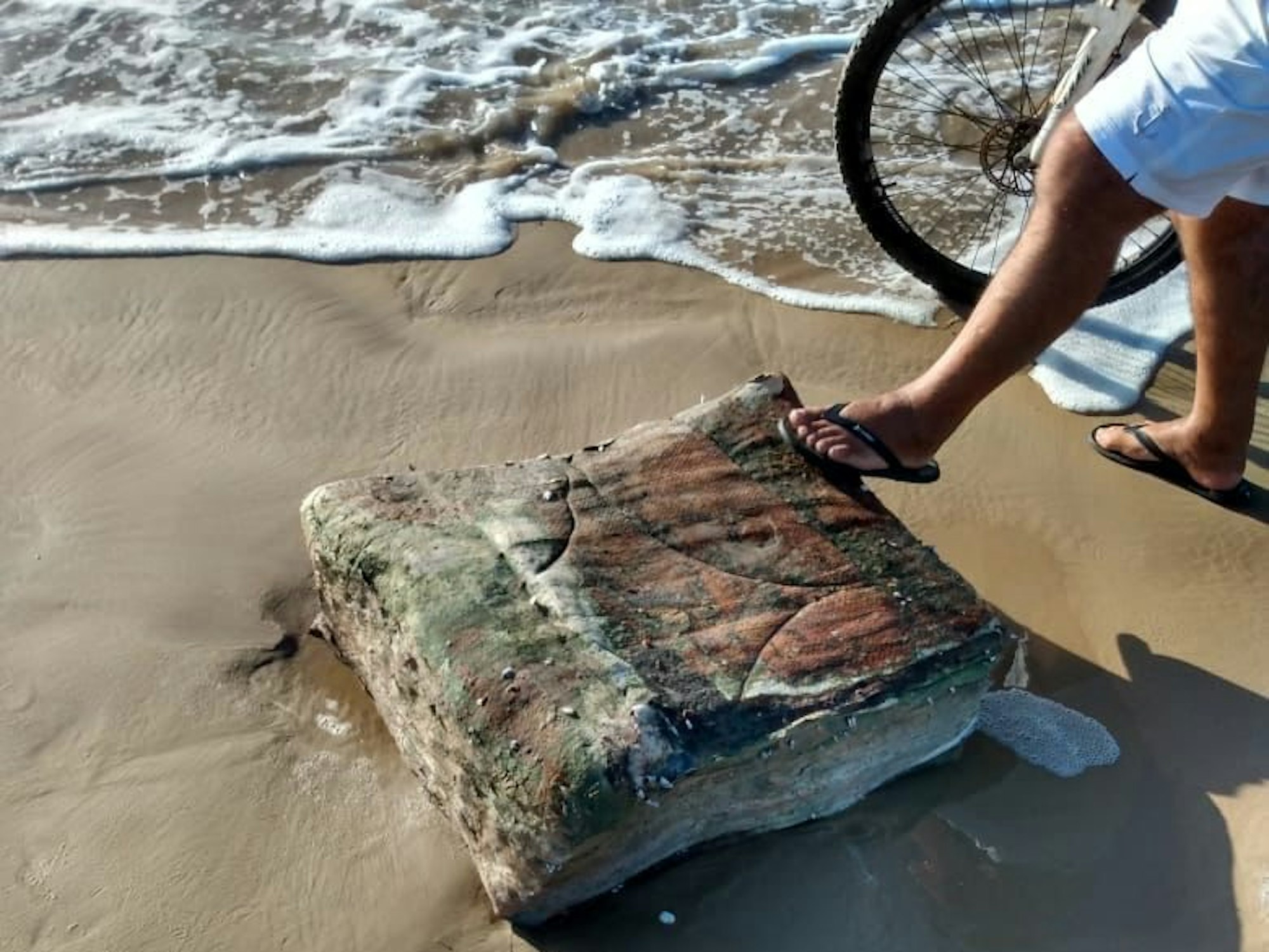 Ein Passant stellt seinen Fuß am Strand von Brasilien auf eine mysteriöse Kiste