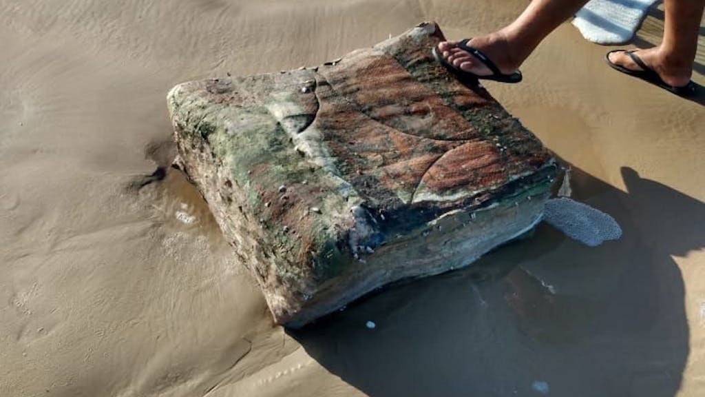 Ein Passant stellt seinen Fuß am Strand von Brasilien auf eine mysteriöse Kiste