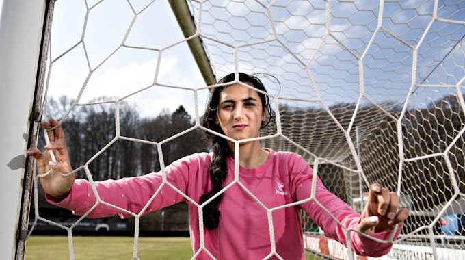 Khalida Popa posiert in einem Tor, sie schaut durch das Tornetz.