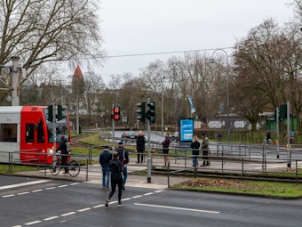 Fußgänger passieren einen Bahnübergang an der Aachener Straße