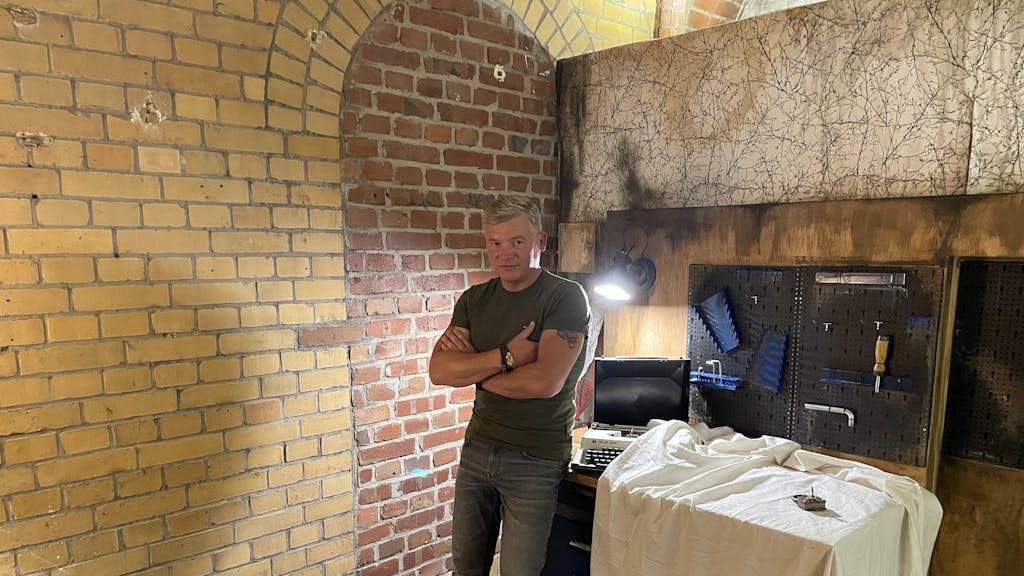 Bestseller-Autor Andreas Winkelmann steht im Escape Room an eine Werkbank angelehnt.