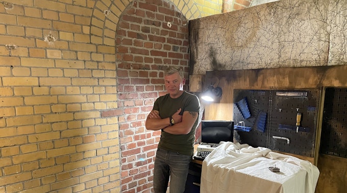 Bestseller-Autor Andreas Winkelmann steht im Escape Room an eine Werkbank angelehnt.