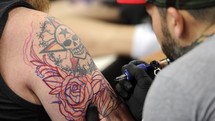 Ein Tätowierer sticht ein Tattoo.