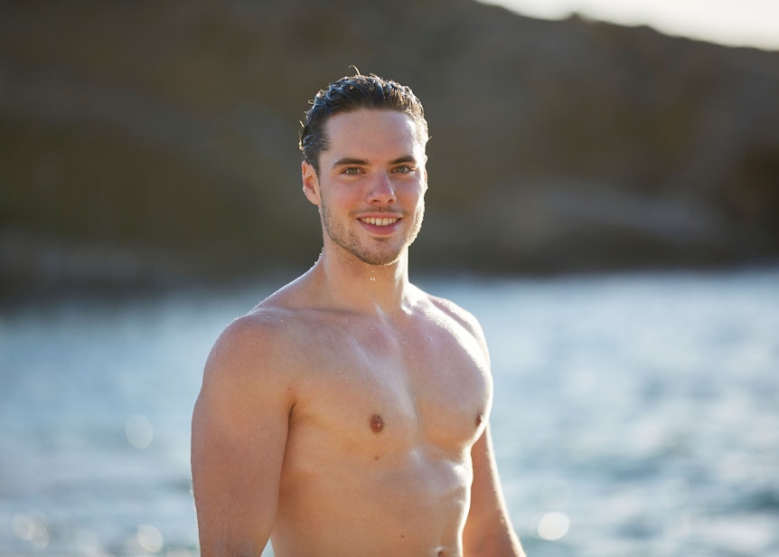 „Bachelorette“-Kandidat Raphael steht im freiem Oberkörper am Strand und lächelt.
