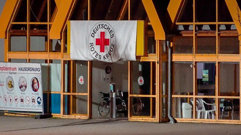 Eine Rot-Kreuz-Fahne hängt über dem Eingang zum Impfzentrum in Eich. Im sächsischen Vogtlandkreis hat es einen Brandanschlag auf ein Impfzentrum gegeben.