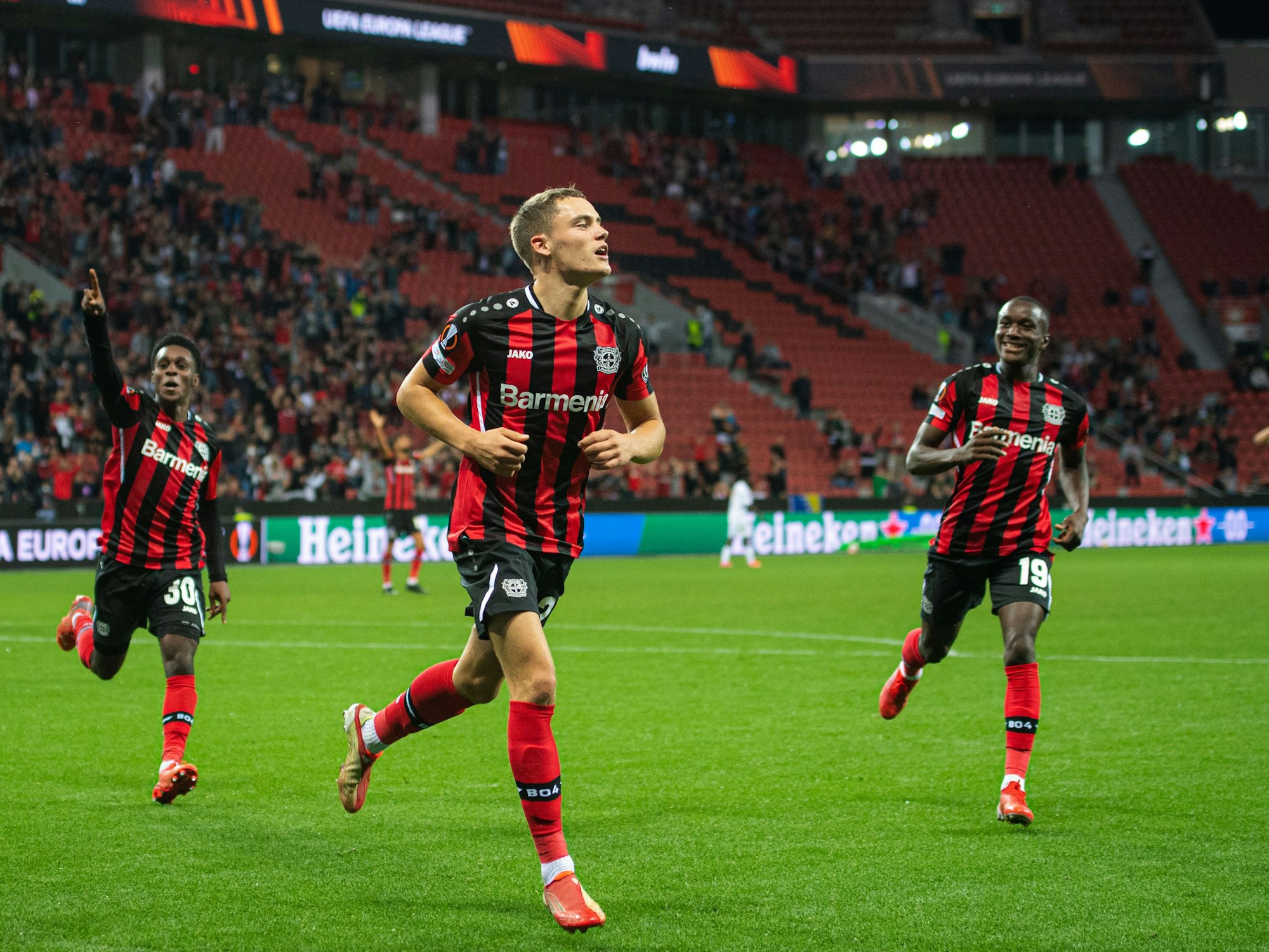 Leverkusens Torschütze Florian Wirtz (M) jubelt nach seinem Treffer zur 2:1 Führung. Daneben laufen Jeremie Frimpong (l) und Moussa Diaby.