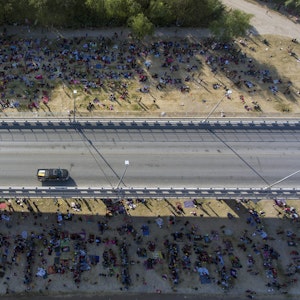 Migranten kampieren unter einer Brücke in Del Rio. Eine Straße ist von oben zu sehen, an der Seite sind unzählige Menschen zu sehen, die dort im Schatten der Brücke verbleiben.