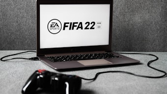Das Logo des am 1. Oktober 2021 erscheinenden Fußball-Konsolen-Spiels FIFA 22 ist auf einem Laptop zu sehen, an den ein Controller angeschlossen ist.