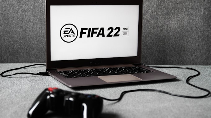 Ein Laptop, auf dem das EA-Logo und der Schriftzug FIFA 22 zu sehen ist. Davor liegt ein Controller.
