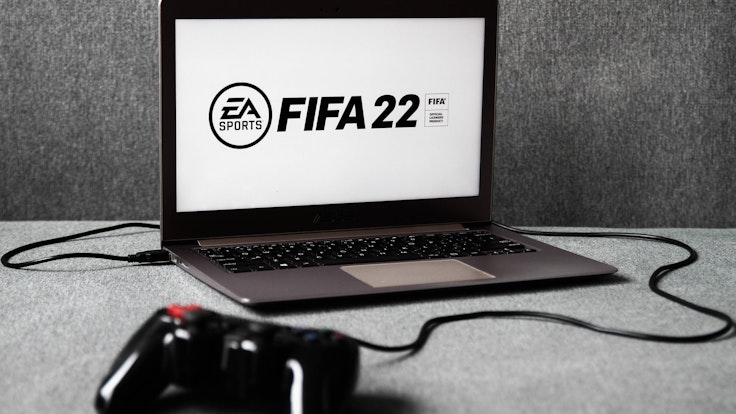 Ein Laptop, auf dem das EA-Logo und der Schriftzug FIFA 22 zu sehen ist. Davor liegt ein Controller.
