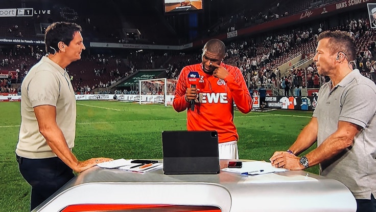 Anthony Modeste weint beim Sky-Interview mit Sebastian Hellmann (l.) und Lothar Matthäus (r.) am 18. September 2021 nach dem 1:1 des 1. FC Köln gegen RB Leipzig.