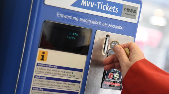 Eine Person wirft Münzen in einen Automaten des Münchner Verkehrs- und Tarifverbunds