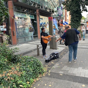 Straßenmusiker singt auf der Straße, ein Passant wirft ihm Geld in den Koffer