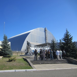 Touristengruppe am Mahnmal vor dem 1986 explodierten Blocks vier des Atomkraftwerks Tschernobyl in der Ukraine. Vor dem geschützten Block steht eine Statue, davor steht eine Gruppe von Touristen.