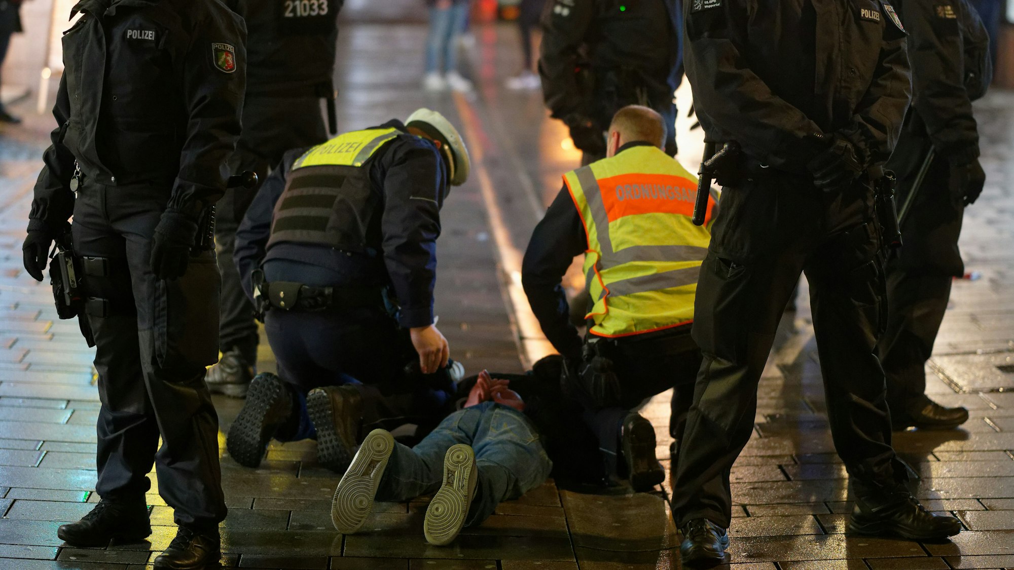 Mitarbeiter des Ordnungsamtes und der Polizei halten am2. Dezember 2020in der Düsseldorfer Altstadt einen bei einer Kontrolle Geflüchteten auf dem Boden fest.