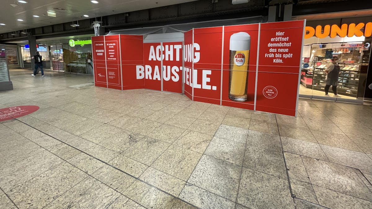 Ein Bauschild mit der Aufschrift „Achtung Braustelle“ steht im Kölner Hauptbahnhof und kündigt das neue Lokal der Brauerei Früh an.