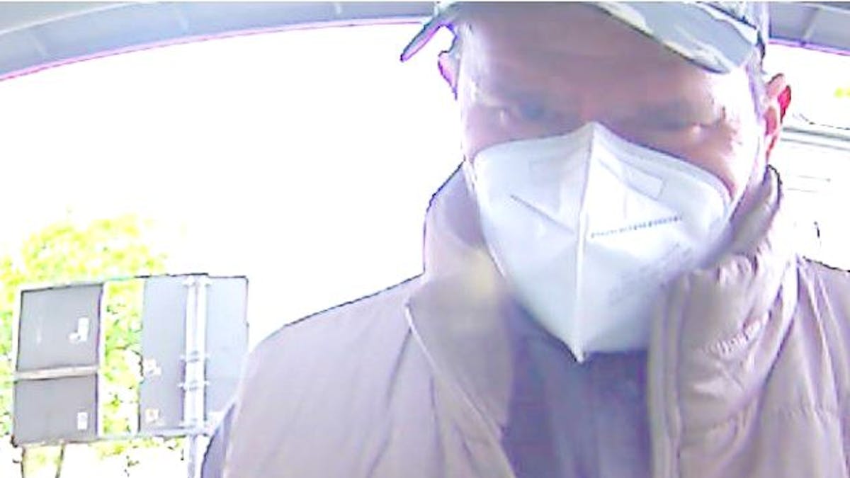 Mann mit Kappe und Corona-Schutzmaske beim Geldabheben am Automaten