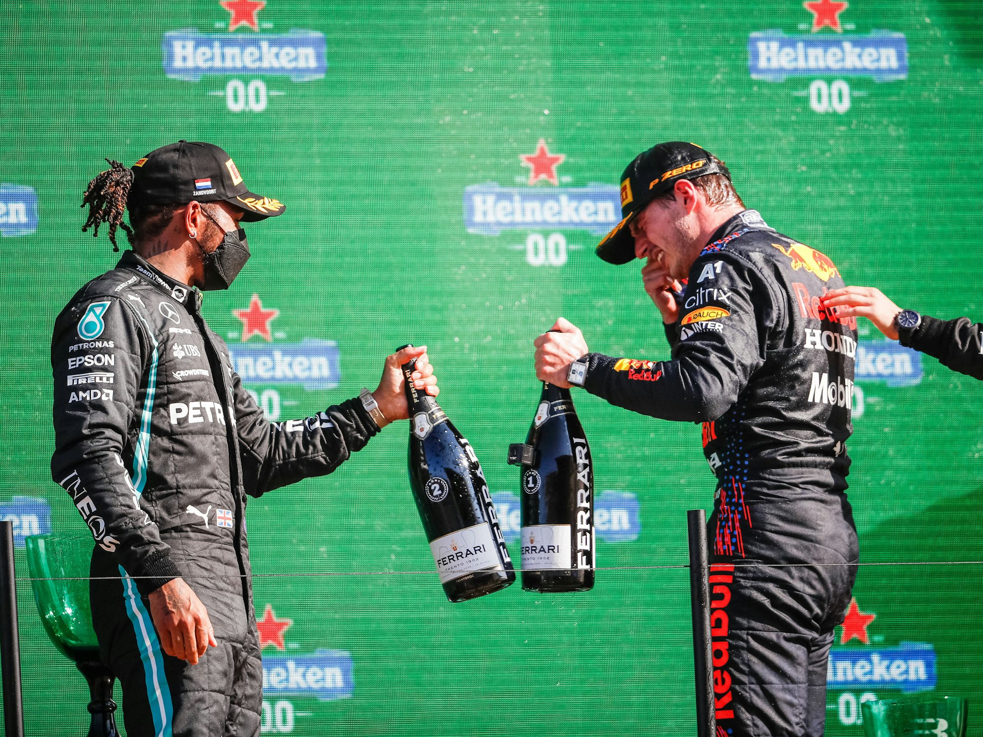 Lewis Hamilton und Max Verstappen stoßen beim Großen Preis der Niederlande auf dem Podium mit Champagner-Flaschen an.