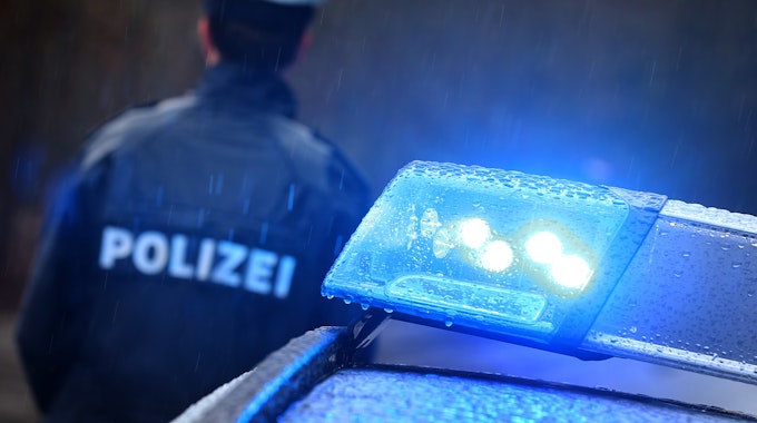 Oberpfalz: Ein Polizist steht im Regen vor einem Streifenwagen dessen Blaulicht aktiviert ist.&nbsp;