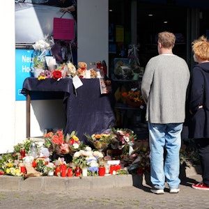 Blumen, Kerzen und Botschaften an das Opfer liegen am 21. September an der Tankstelle in der Innenstadt von Idar-Oberstein. Menschen stehen davor mit gefalteten Händen und gedenken des Opfers.