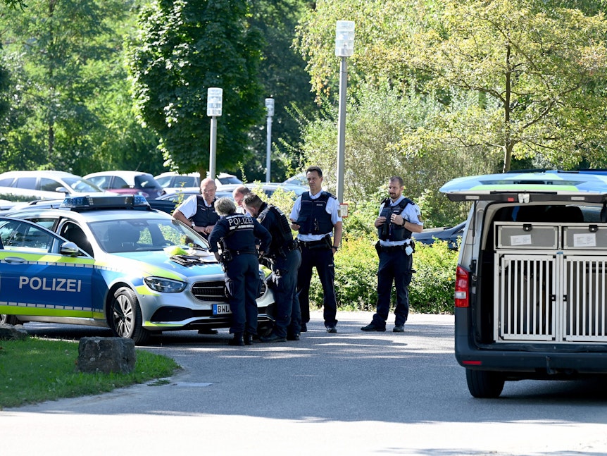 Polizisten besprechen sich vor der Klinik am Weissenhof, sie haben eine Karte auf der Motorhaube ausgebreitet. Auch ein Wagen mit einer Box für einen Spürhund ist zu sehen.