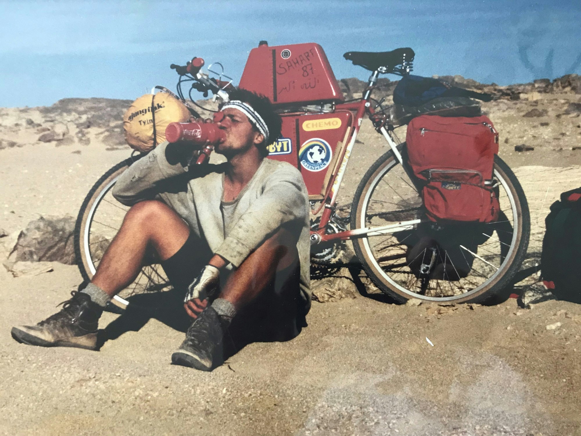 Dieter Wolfs Sohn sitzt in der Wüste vor einem Fahrrad und trinkt.