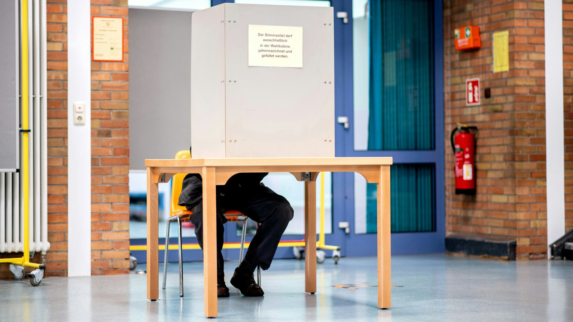Ein Wähler sitzt in einem Wahllokal, das im Foyer einer Grundschule untergebracht ist, in der Wahlkabine und füllt seinen Stimmzettel für die Kommunalwahl aus.