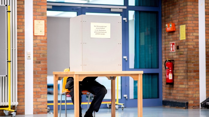 Ein Wähler sitzt in einem Wahllokal, das im Foyer einer Grundschule untergebracht ist, in der Wahlkabine und füllt seinen Stimmzettel für die Kommunalwahl aus.