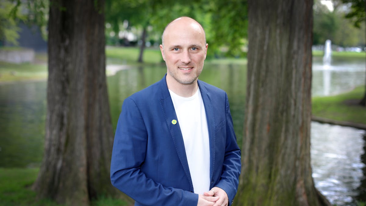 Sven Lehmann steht vor einem See mit Bäumen und lächelt in die Kamera.