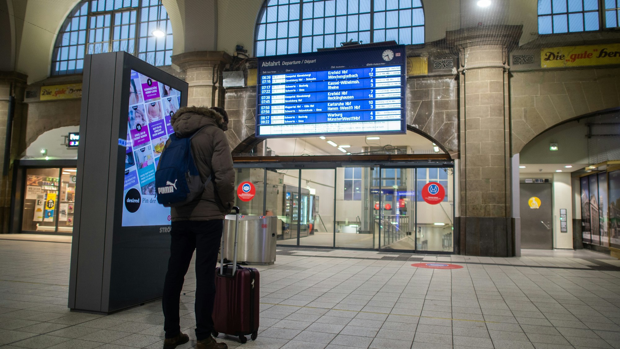 Ein Mann steht im Hauptbahnhof vor der Anzeigetafel, auf der Verspätungen und Zugausfälle angezeigt werden, und schaut auf sein Smartphone.