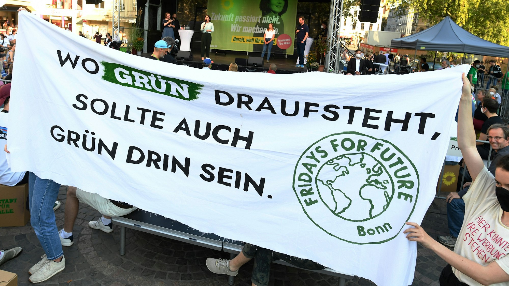 Aktivistinnen von Fridays for Future halten ein Transparent mit der Aufschrift «Wo Grün draufsteht, sollte auch Grün drin sein.», während der Rede von Annalena Baerbock (hinten).