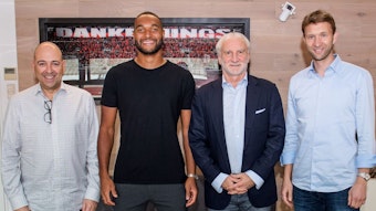 Jonathan Tah posiert zusammen mit Geschäftsführer Fernando Carro, Rudi Völler und Simon Rolfes vor einem Bild, das im Stadion aufgenommen worden ist.