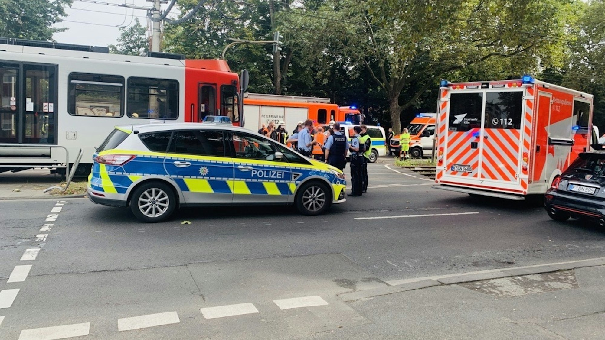 Einsatzfahrzeuge von Polizei, Feuerwehr und Rettungsdienst stehen auf der Straße, außerdem ein Pulk von Einsatzkräften. Eine Straßenbahn hat gestoppt.