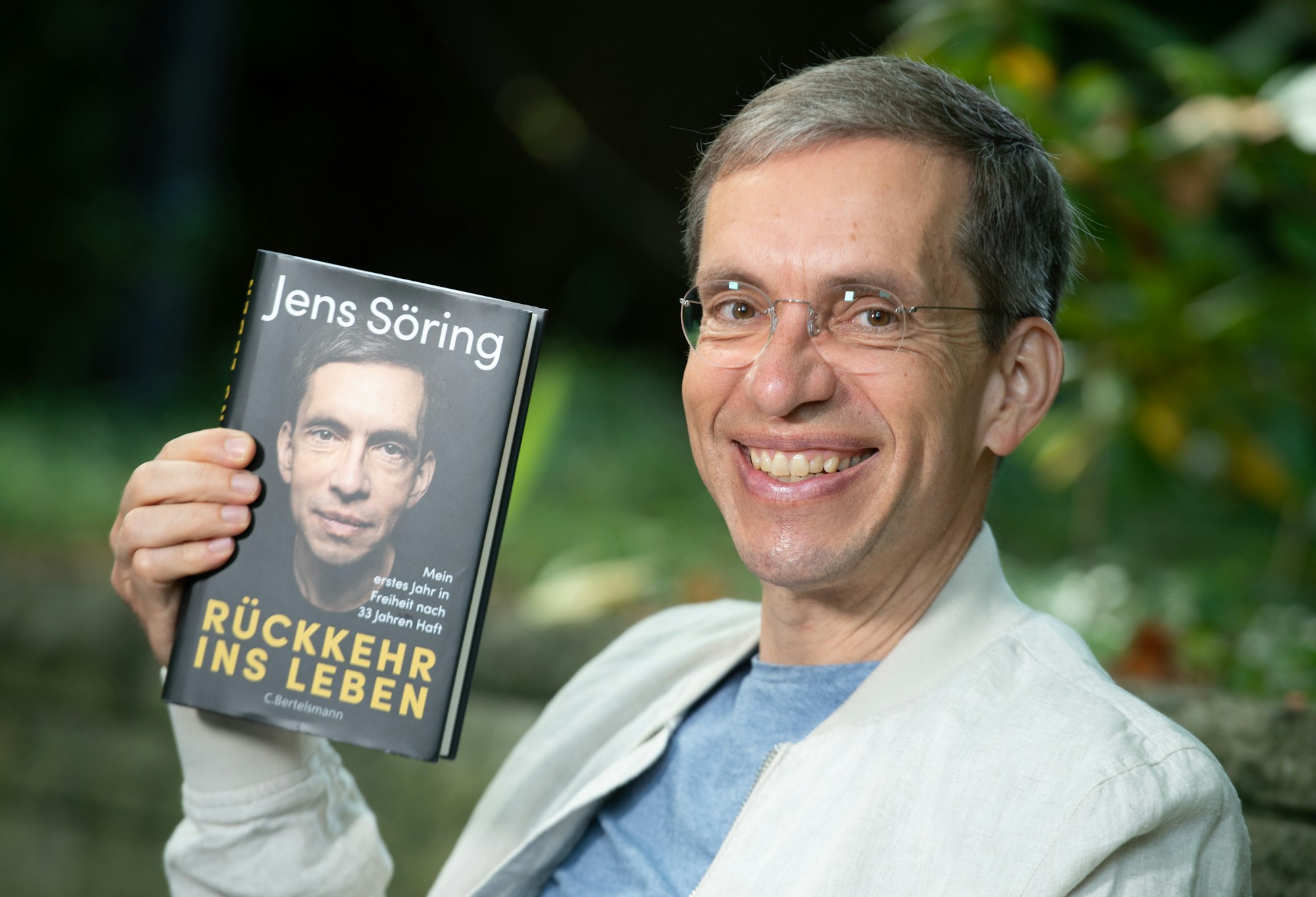 Jens Söring hält sein Buch in der Hand und lächelt in die Kamera.