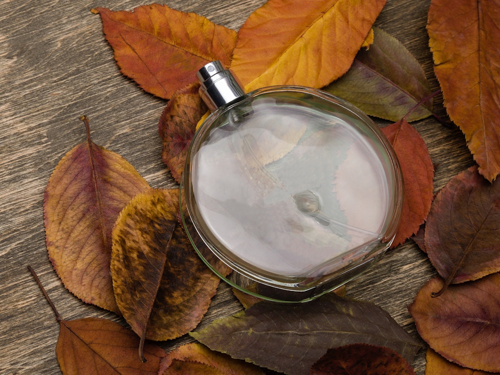 Eine Parfümflasche liegt auf Herbstlaub.