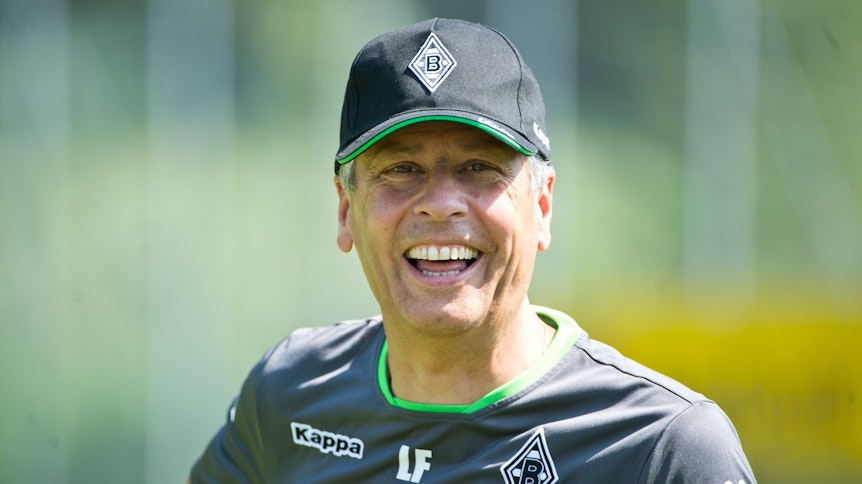 Lucien Favre lächelt als Trainer von Fußball-Bundesligist Borussia Mönchengladbach am 17. Juli 2015 während des Trainingslagers in Rottach-Egern (Bayern) in die Kamera. Er trägt dabei ein Kappe auf dem Kopf.