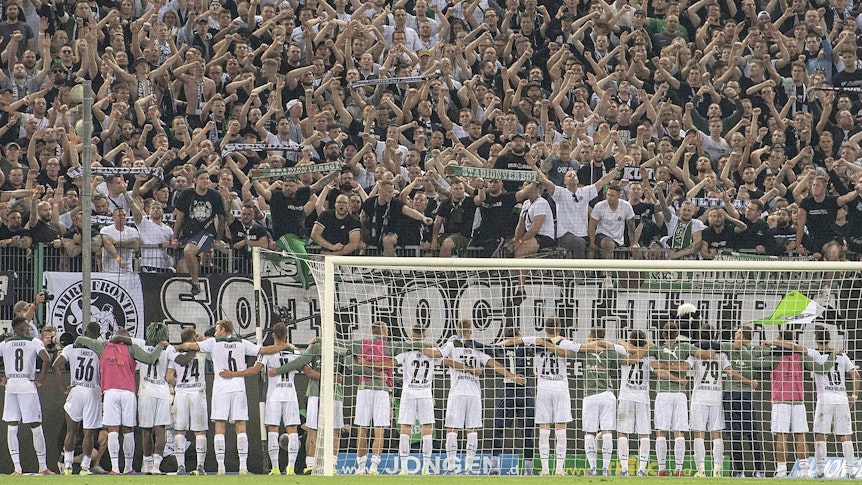 Spieler und Fans von Fußball-Bundesligist Borussia Mönchengladbach feiern gemeinsam nach dem siegreichen Duell gegen Dortmund am 25. September 2021 im Borussia-Park. Die Gladbacher Spieler umarmen sich und stehen vor der Fankurve.