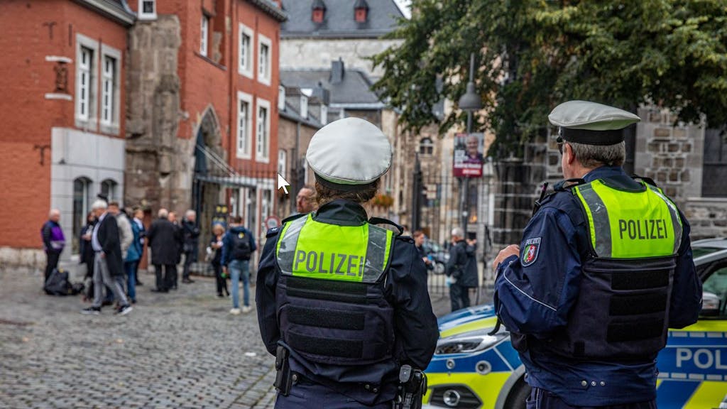 Zwei Polizisten stehen neben einem Einsatzwagen vor dem Aachener Dom.&nbsp;