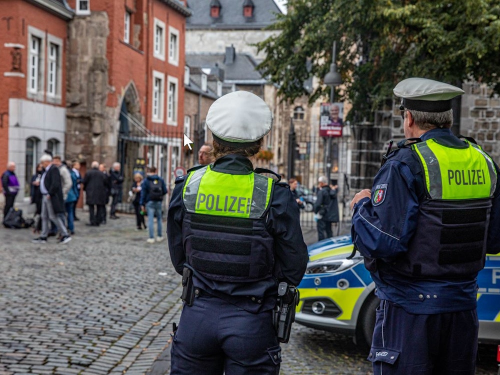 Zwei Polizisten stehen neben einem Einsatzwagen vor dem Aachener Dom.
