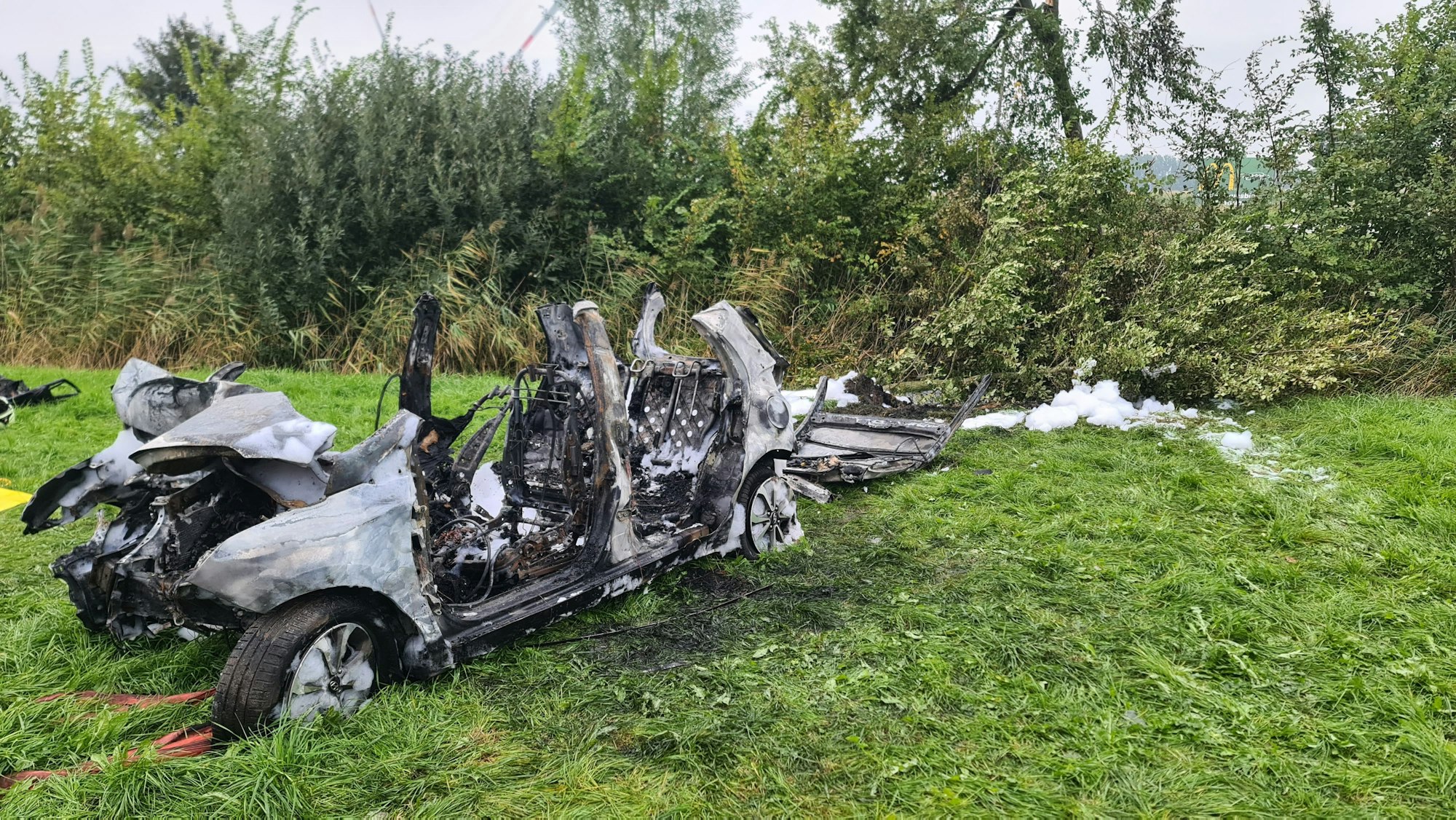 Das ausgebrannte Wrack eines Autos steht am 02.10.2021 am Fahrbahnrand. Drei junge Menschen sind bei dem Autounfall in Brunsbüttel im Kreis Dithmarschen verbrannt.