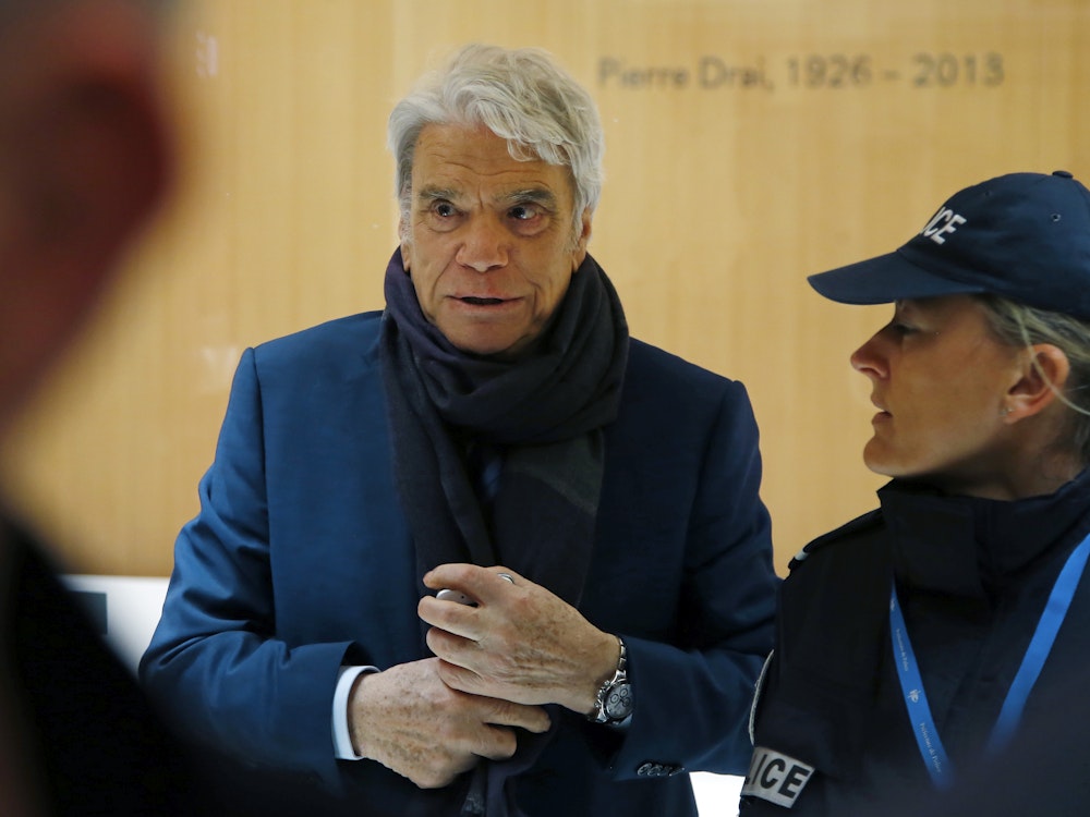 Bernard Tapie (l.), früherer Adidas-Eigner sowie Minister, Schauspieler und Fußballmanager, kommt in Begleitung einer Polizistin an einem Pariser Gericht an.