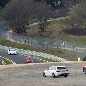 Das Symbolbild zeigt die Nordschleife des Nürburgrings im April 2021, mehrere Autos fahren auf der Strecke, einige Menschen stehen am Rand und schauen zu.