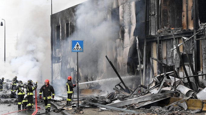 Ein Kleinflugzeug stürzt in Mailand am Sonntag (3. Oktober) nur Augenblicke nach dem Start ab und in ein Bürogebäude. Feuerwehrleute löschen die Trümmer des Gebäudes, Qualm steigt auf.