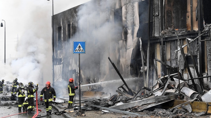 Ein Kleinflugzeug stürzt in Mailand am Sonntag (3. Oktober) nur Augenblicke nach dem Start ab und in ein Bürogebäude. Feuerwehrleute löschen die Trümmer des Gebäudes, Qualm steigt auf.