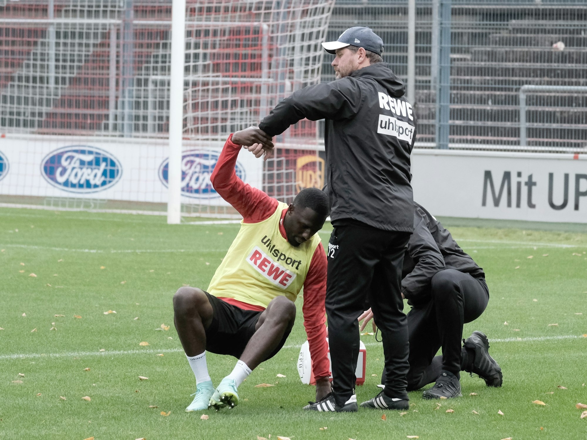 Steffen Baumgart hilft dem angeschlagenen Kingsley Schindler im Training des 1. FC Köln auf die Beine.
