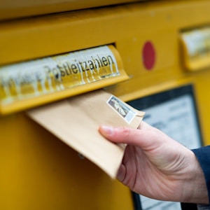Das Symbolbild zeigt einen Mann, der einen Brief in einen Briefkasten wirft.