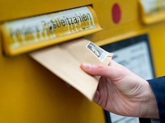 Das Symbolbild zeigt einen Mann, der einen Brief in einen Briefkasten wirft.
