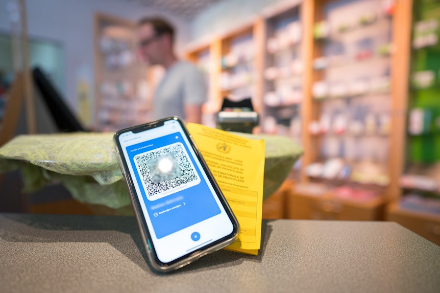 Ein Smartphone mit dem QR Code eines digitalen Impfausweises liegt zusammen mit einem Impfbuch auf dem Tisch einer Apotheke.