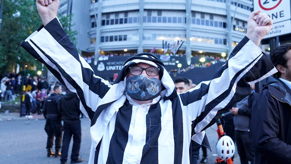 Ein Fan von Newcastle trägt eine arabische Kopfbedeckung und streckt die Arme zum Jubeln in die Höhe.